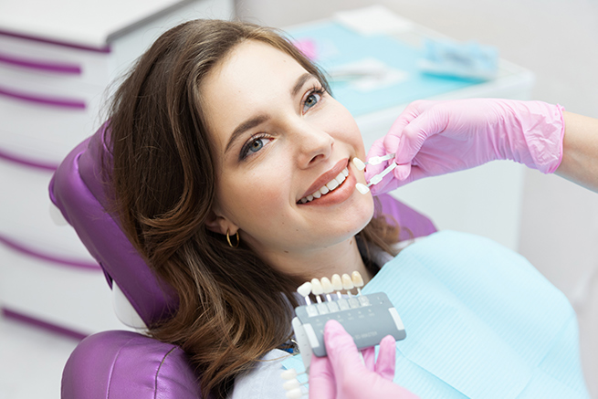 Patient getting a checkup on teeth color to match hers, Dentist holding tooth color samples