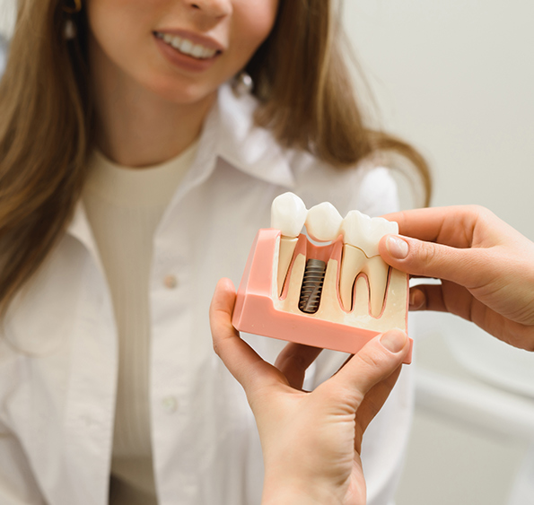 Patient smiling in the background, Hand of dentist holding anatomy toy to show the dental implant procedure