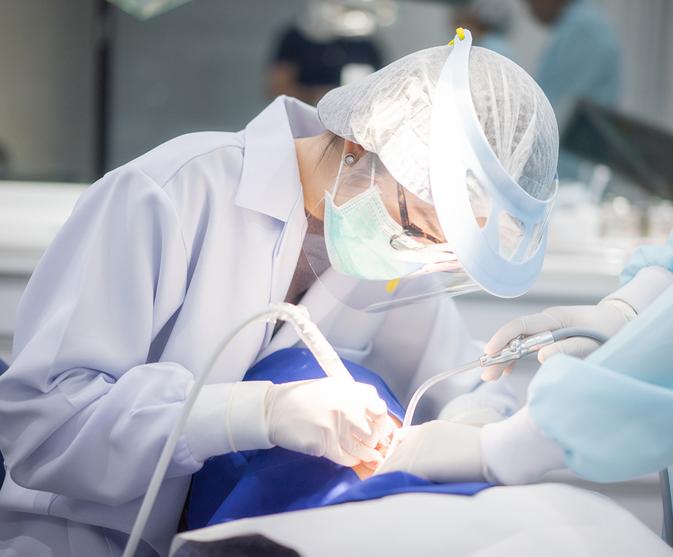 Dentist performing surgery on a patient, Dentist wearing eye glasses and face shield