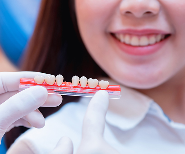Woman in background smiling, Hand of dentist showing different shape of tooth